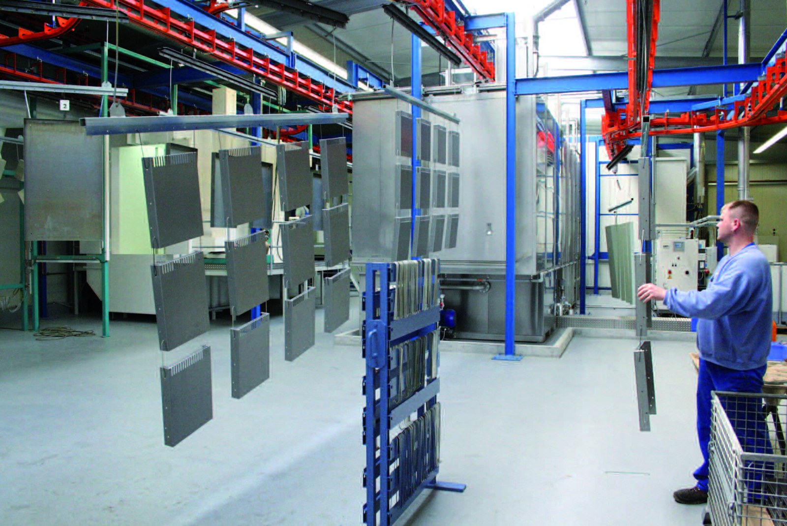 Mitarbeiter neben aufgehängten Bauteilen und roter Fördertechnik bei Henke