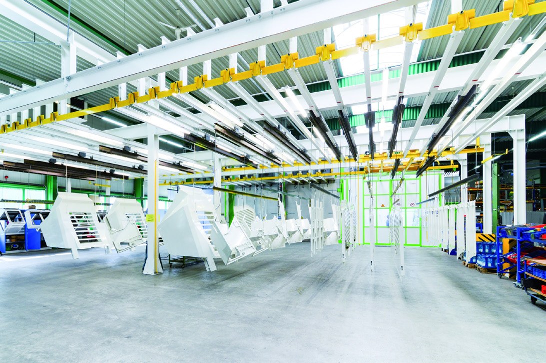 Beschichtungsanlage bei Hennecke mit aufgehängten weißen Bauteilen und gelber Fördertechnik